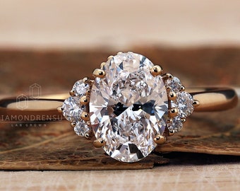 Puede incluir: Un anillo de compromiso de oro con un diamante central de forma ovalada y diamantes más pequeños engastados a su alrededor. El anillo está sobre una superficie de madera.