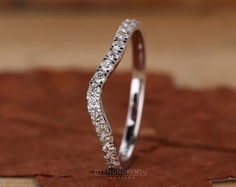 Puede incluir: Una fina banda de boda curvada con una fila de pequeños diamantes brillantes engastados en una banda de metal blanco.