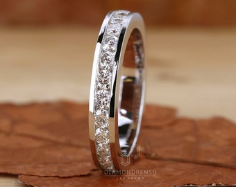 May include: A thin silver band with a row of small, clear diamonds set in a channel setting. The band is polished and has a smooth finish.  "DIAMONDRENSU LAB GROWN" is printed on the band.