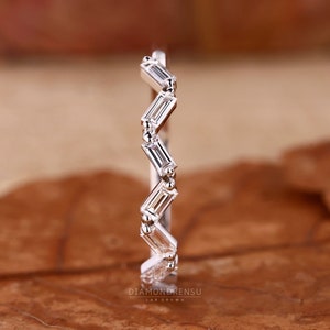 May include: A silver ring with a zigzag design. The ring features rectangular, clear stones set between small, round beads. The ring is on a brown surface. The text "DIAMONDRENSU LAB GROWN" is at the bottom.