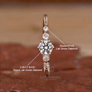 K&ouml;nnte beinhalten: Ein Goldring mit einem runden, im Labor gez&uuml;chteten Diamanten von 0,29 Karat in der Mitte und kleineren, runden, im Labor gez&uuml;chteten Diamanten auf der Ringschiene. Der Ring ist mit "DIAMONDRENSU LAB GROWN" beschriftet.