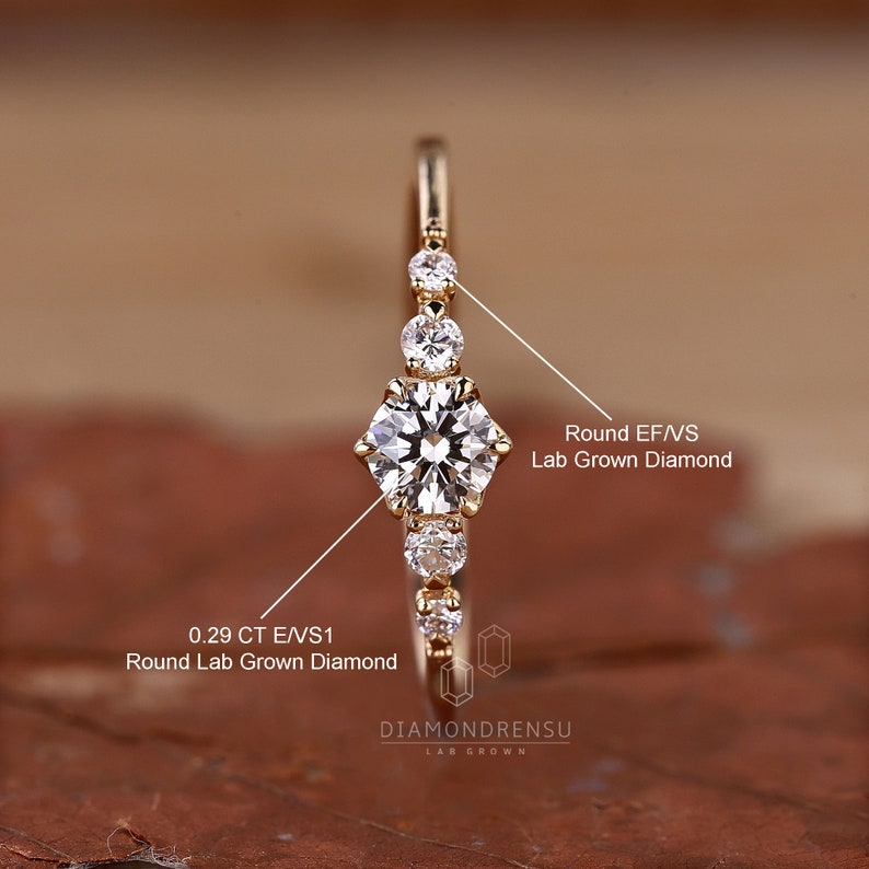 K&ouml;nnte beinhalten: Ein Goldring mit einem runden, im Labor gez&uuml;chteten Diamanten von 0,29 Karat in der Mitte und kleineren, runden, im Labor gez&uuml;chteten Diamanten auf der Ringschiene. Der Ring ist mit "DIAMONDRENSU LAB GROWN" beschriftet.
