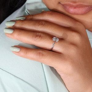 May include: A silver ring with a large oval-shaped diamond set in a halo of smaller diamonds. The ring is on a person's finger.