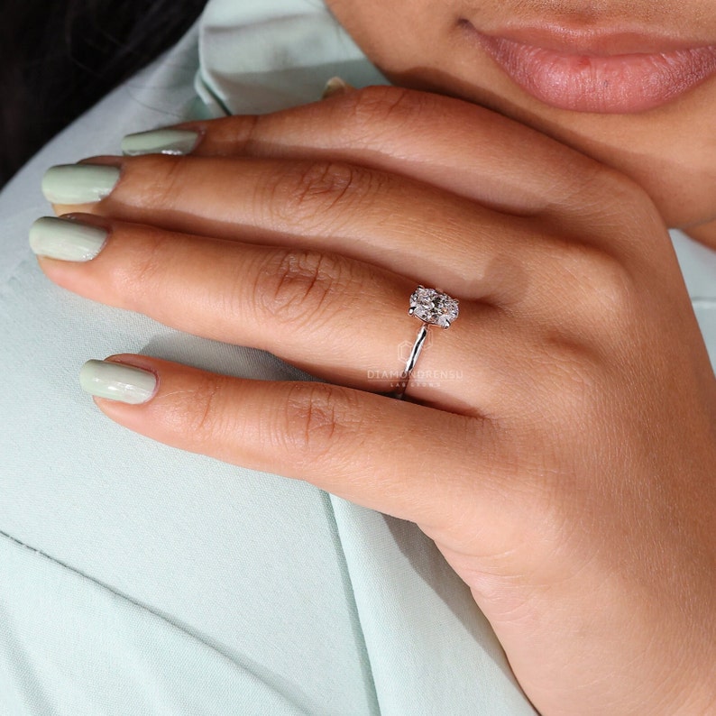 May include: A silver ring with a large oval-shaped diamond set in a halo of smaller diamonds. The ring is on a person's finger.