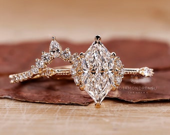 May include: A gold engagement ring set with a large, clear, marquise-shaped diamond centre stone. The ring is accented with smaller diamonds in a delicate, floral design. The band is also set with smaller diamonds. The ring is on a wooden surface. "DIAMONDRENSU LAB GROWN" is printed on the surface.