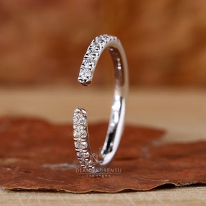 May include: A delicate, open-ended, white gold ring with a band of small, sparkling diamonds.