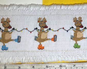 Puede incluir: Tela blanca con tres renos bordados que llevan botas y sostienen cadenas de luces navideñas. La tela está etiquetada con "Item#: 286 Description: reindeer in boots QTY:"