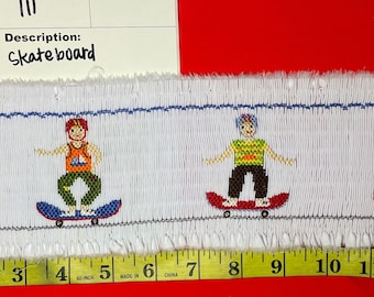 Puede incluir: Tela blanca bordada con tres niños en patinetas. La tela mide 16 pulgadas de largo y tiene un borde azul. Los niños llevan camisas y pantalones de diferentes colores. El texto "Item#: 111 QTY: Description: Skateboard" está impreso en una etiqueta blanca.