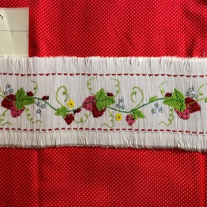May include: White fabric with a red embroidered strawberry vine design. The fabric has a fringed edge. The fabric is labeled "Item # 001 Description: strawberry vine"