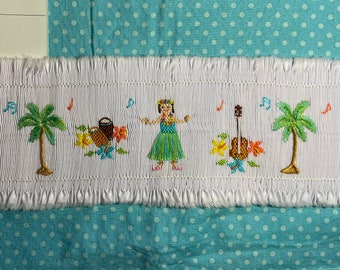 Puede incluir: Tela blanca con ribete de volantes y un diseño bordado de una bailarina de hula, palmeras, notas musicales y un ukelele. La tela tiene el texto "Item # 004" y "Description: Hawaii hula" en una etiqueta amarilla.