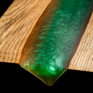 May include: Close-up of a wooden board with a green epoxy resin river flowing through it. The resin has a sparkly finish.