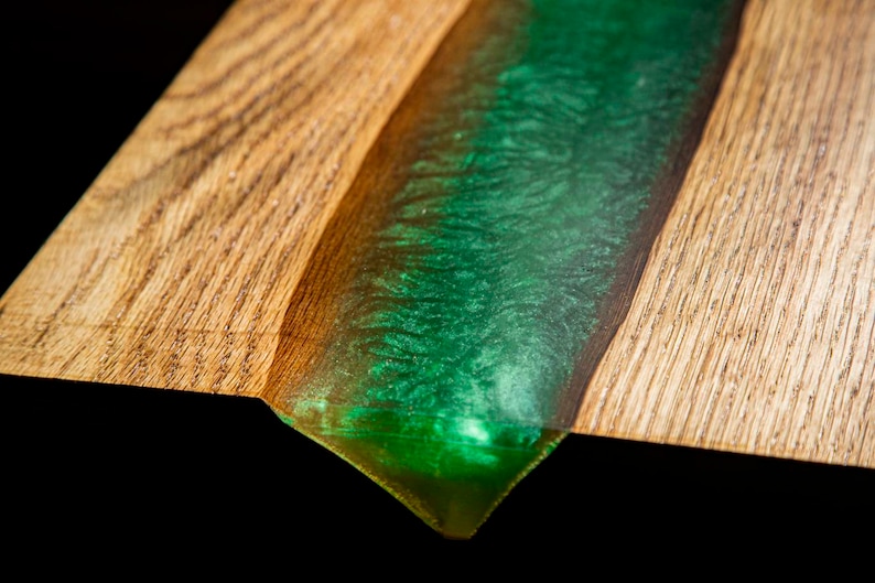 May include: Close-up of a wooden board with a green epoxy resin river flowing through it. The resin has a sparkly finish.