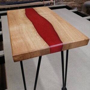 May include: A wooden coffee table with a red epoxy resin river running through the center. The table has black hairpin legs.