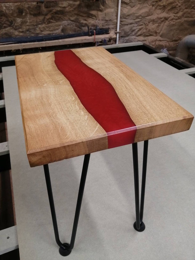 May include: A wooden coffee table with a red epoxy resin river running through the center. The table has black hairpin legs.