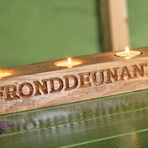 May include: Wooden candle holder with three candle slots and the text "FRONDDEUNANT" engraved on the front. The holder is made of natural wood and has a rustic look.
