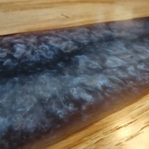 May include: Close-up of a wooden table top with a dark blue and white epoxy resin inlay. The resin has a swirling, marbled effect.