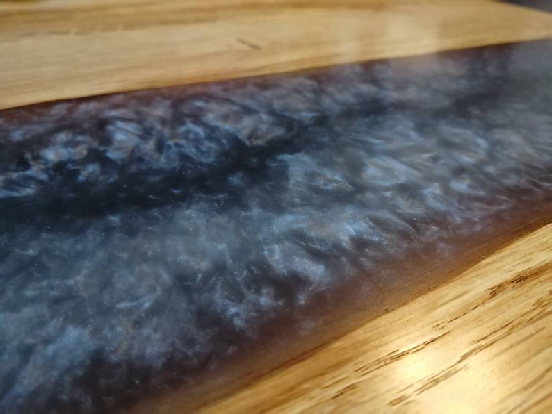 May include: Close-up of a wooden table top with a dark blue and white epoxy resin inlay. The resin has a swirling, marbled effect.