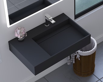 May include: A black floating bathroom vanity with a white porcelain sink and a chrome faucet. The vanity is mounted on a white wall and has a small flower arrangement on the side. A wicker basket is underneath the vanity.