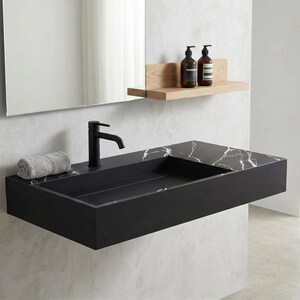 May include: A modern black floating bathroom sink with a marble-patterned top. A black faucet is installed on the sink, and a rolled gray towel rests on the side. A wooden shelf holds two brown bottles. A large mirror is above the sink.