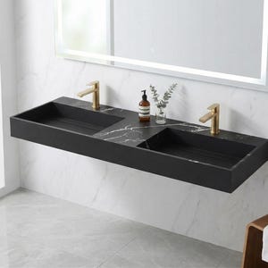 May include: A modern, wall-mounted double sink in black with gold-colored faucets. The sink has a marble-like pattern and is mounted on a white wall. A mirror and accessories are also visible.