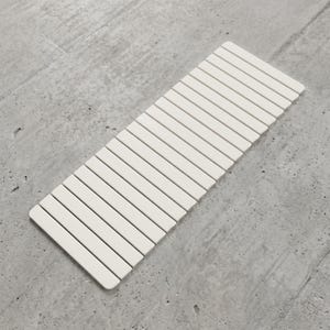 May include: A rectangular, off-white, segmented mat composed of numerous parallel, rounded-edge slats. The mat is positioned diagonally against a gray, textured surface, creating a clean, minimalist aesthetic. The mat's design suggests a kitchen or bathroom accessory.