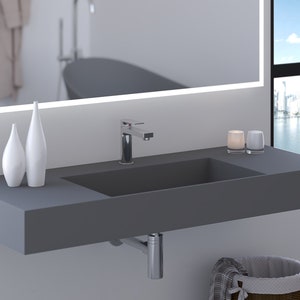 May include: A modern, gray bathroom sink with a rectangular basin and a chrome faucet. Two white decorative vases and two small glass candle holders sit on the countertop. A large mirror with a light frame is above the sink.