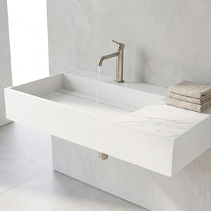 May include: A modern, rectangular white bathroom sink with a built-in countertop and a brushed nickel faucet. Water flows from the faucet into the sink. A stack of beige towels rests on the countertop. The sink is mounted on a white wall.