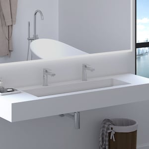 May include: A modern white bathroom vanity with a rectangular sink and two chrome faucets. A large mirror reflects a bathtub and a window with a city view. A tray with accessories sits on the counter, and a wicker basket is below.