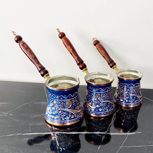 May include: Three blue and copper Turkish coffee pots with intricate floral designs and wooden handles.