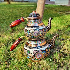 Puede incluir: Un juego de té turco tradicional con base de cobre y diseños florales coloridos. La tetera tiene dos secciones y un mango de madera.