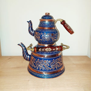 Puede incluir: Un juego de té turco tradicional con un diseño floral azul y dorado. La tetera tiene una base de cobre y un mango de madera. El juego está hecho de metal y es perfecto para preparar té.