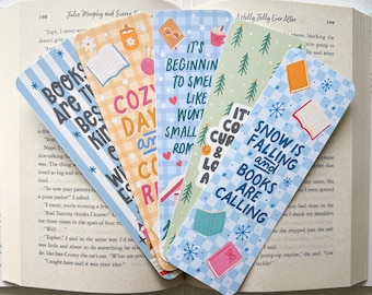 May include: Set of six colorful bookmarks with different winter-themed illustrations and text. The bookmarks feature a blue and white checkered pattern, snowflakes, and text such as "It's beginning to smell like winter" and "Snow is falling and books are calling".