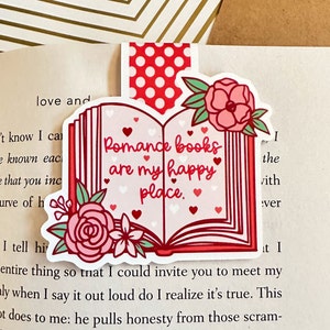 May include: A pink and red bookmark with a book design and the text "Romance books are my happy place." The bookmark has a white background with pink and red hearts and flowers.