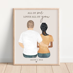 May include: A framed print with a watercolor illustration of a couple standing back to back. The text "ALL OF me LOVES ALL OF you" is written in a cursive font. The couple's names "JACOB & MIA" are written below the illustration with a heart symbol.