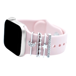 Może przedstawiać: Różowy pasek do Apple Watch z srebrnymi zawieszkami w kształcie półksiężyca, gwiazdy i linii gwiazd. Zawieszki są przymocowane do paska małymi srebrnymi pętlami.