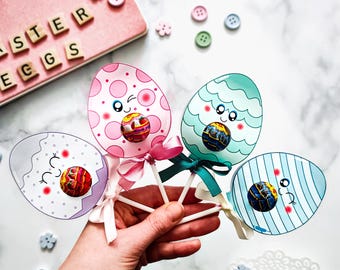 May include: Three Easter egg lollipops with cute faces and candy inside. The eggs are pink with white polka dots, blue with white stripes, and purple with white dots.