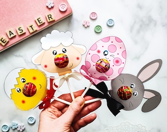 May include: Three Easter-themed lollipop crafts. A pink and white egg, a gray bunny, and a white sheep. Each craft has a lollipop attached to the back.