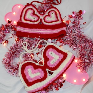May include: Two crocheted heart-shaped tops in red, pink, and white. The tops are made with a chunky yarn and have a simple, minimalist design.