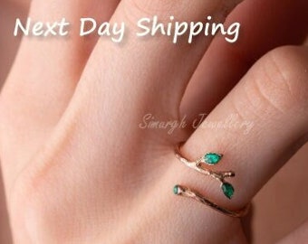 May include: Gold ring with a delicate branch design and green gemstone leaves.  The ring is shown on a finger.