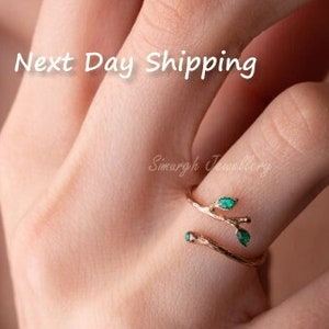 May include: Gold ring featuring a delicate branch design with green gemstone leaves. The ring is displayed on a finger.