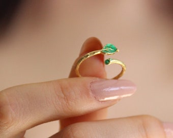 May include: A gold ring with two small green gemstones. The ring is open and wraps around the finger.