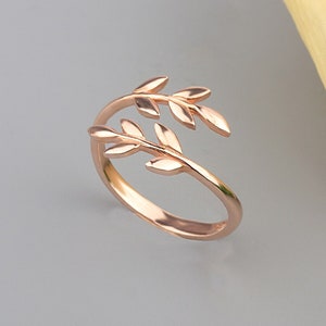 May include: A rose gold ring featuring a delicate design of two intertwined branches with leaves.