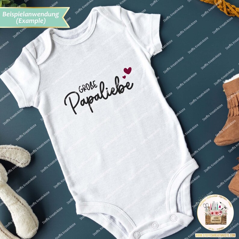 May include: White baby onesie with black text that reads "GROBE Papaliebe" with two small red hearts above the text.