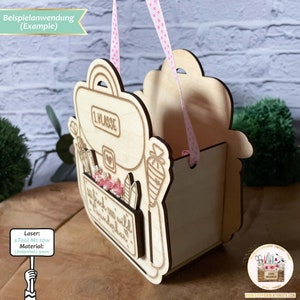 May include: A wooden backpack-shaped box with a pink ribbon handle. The box is decorated with the words "1. Klasse" and a small heart. The box is made of 3mm linden wood and was cut with an xTool M1 10W laser.