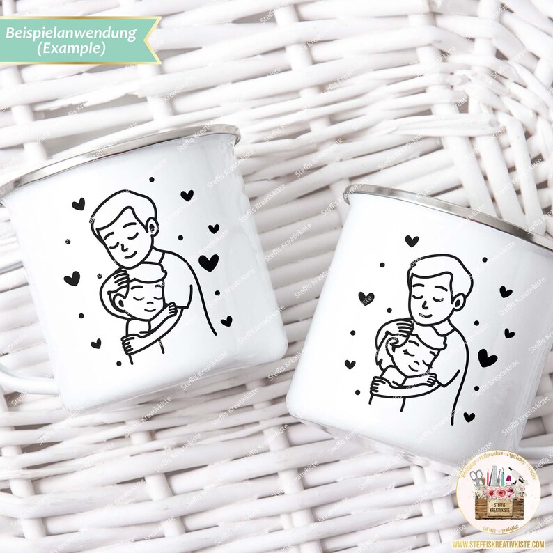 May include: Two white enamel mugs with black outlines of a father and child hugging. The mugs have black hearts scattered around the image. The text "Beispielanwendung (Example)" is at the top of the image.
