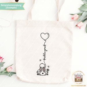 May include: A white tote bag with a black and white illustration of a bunny holding a heart-shaped balloon. The text "fr&uuml;hlingsgr&uuml;&szlig;e" is written vertically on the balloon string.