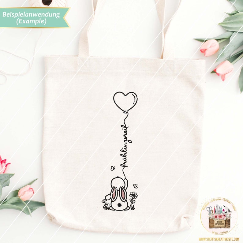 May include: A white tote bag with a black and white illustration of a bunny holding a heart-shaped balloon. The text "fr&uuml;hlingsgr&uuml;&szlig;e" is written vertically on the balloon string.