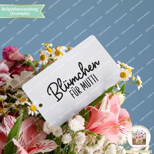 May include: A white card with black text that reads "Bl&uuml;mchen f&uuml;r Mutti" (Flowers for Mom) is placed in a bouquet of white and pink flowers.