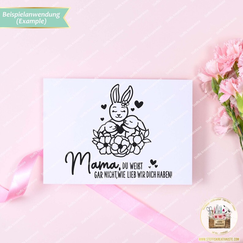 May include: A black and white illustration of a bunny rabbit holding two smaller bunnies with the text "Mama, du weist gar nicht, wie lieb wir dich haben!"  The illustration is surrounded by a wreath of flowers.