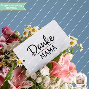 K&ouml;nnte beinhalten: Eine wei&szlig;e Karte mit schwarzem Text, auf der "Danke Mama" mit einem kleinen rosa Herzen &uuml;ber dem Wort "Mama" steht. Die Karte liegt auf einem Strau&szlig; rosa und wei&szlig;er Blumen.